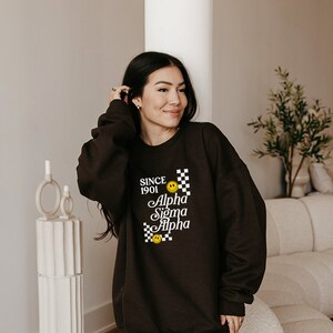 May include: A black sweatshirt with a white graphic design that says "Since 1901 Alpha Sigma Alpha" with a chequered pattern and smiley faces.