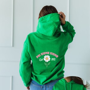 May include: Green hooded sweatshirt with a white daisy and the text "Phi Sigma Sigma Est 1913" printed on the back.