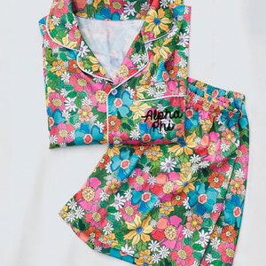 Puede incluir: Un conjunto de pijama de estampado floral con ribete blanco. La parte superior tiene cierre de botones y los pantalones cortos tienen cintura elástica. Los pantalones cortos tienen el texto "Alpha Phi" bordado en la parte delantera.