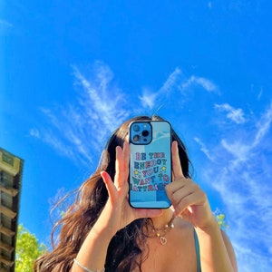 May include: A person is holding a blue and white phone case with the text "Be the energy you want to attract" in colourful letters. The phone case has a white background with a blue and white design.