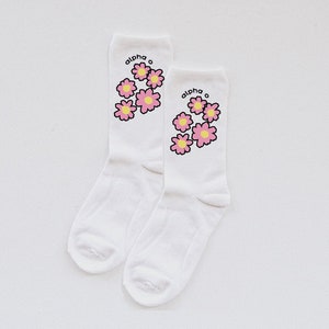 May include: A pair of white socks with a pink and yellow flower design and the text "alpha o" on each sock.