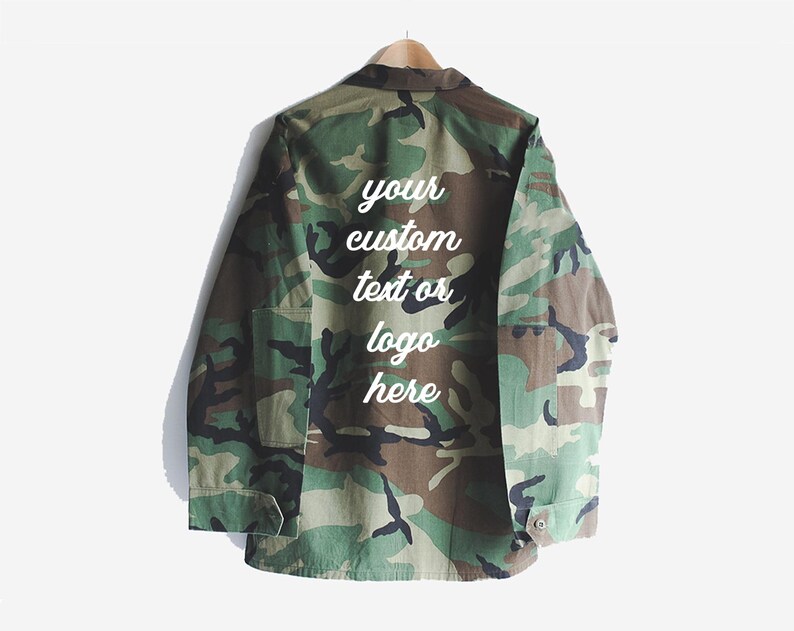 Puede incluir: Una chaqueta utilitaria de color verde camuflaje con un mensaje bordado en blanco en la parte posterior que dice "your custom text or logo here".