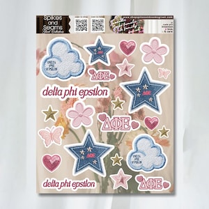 Puede incluir: Una hoja de pegatinas con varias formas, incluyendo estrellas, corazones, nubes y flores. Las pegatinas son de color azul, rosa y dorado, con el texto "Delta Phi Epsilon" y "Spikes and Seams".