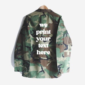 Puede incluir: Una chaqueta utilitaria de color verde camuflaje con texto blanco en la parte posterior que dice "we print your text here".