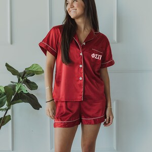 Puede incluir: Un conjunto de pijama de satén rojo con ribetes blancos y las letras griegas "ΦΣΠ" bordadas en la camisa.
