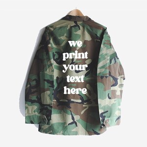 May include: A camouflage green jacket with a white print on the back that says "we print your text here".