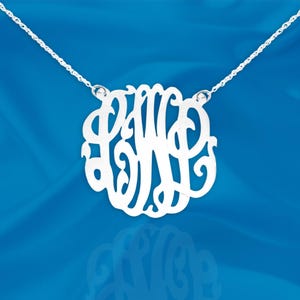 May include: A silver necklace with a delicate chain and a large, openwork monogram pendant. The pendant features the letters "PWB" in a stylized script font.