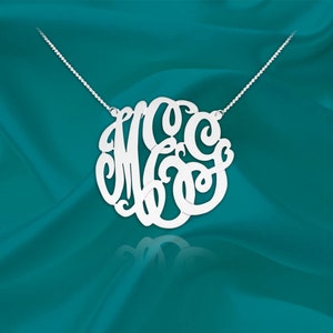 May include: A silver necklace with a large, circular monogram pendant featuring the letters "MGC" in a cursive script.