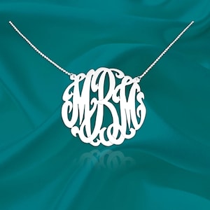 May include: A silver necklace with a large, circular monogram pendant featuring the letters "MRM" in a script font.
