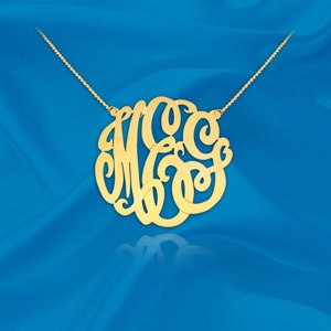 Puede incluir: Un collar dorado con un gran colgante circular que presenta un monograma de las letras M, C y G. El colgante está hecho de un diseño delicado y calado.