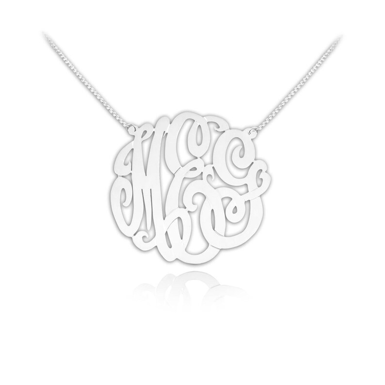 May include: Silver necklace with a large, circular monogram pendant featuring the letters M, C, and G in a cursive script.