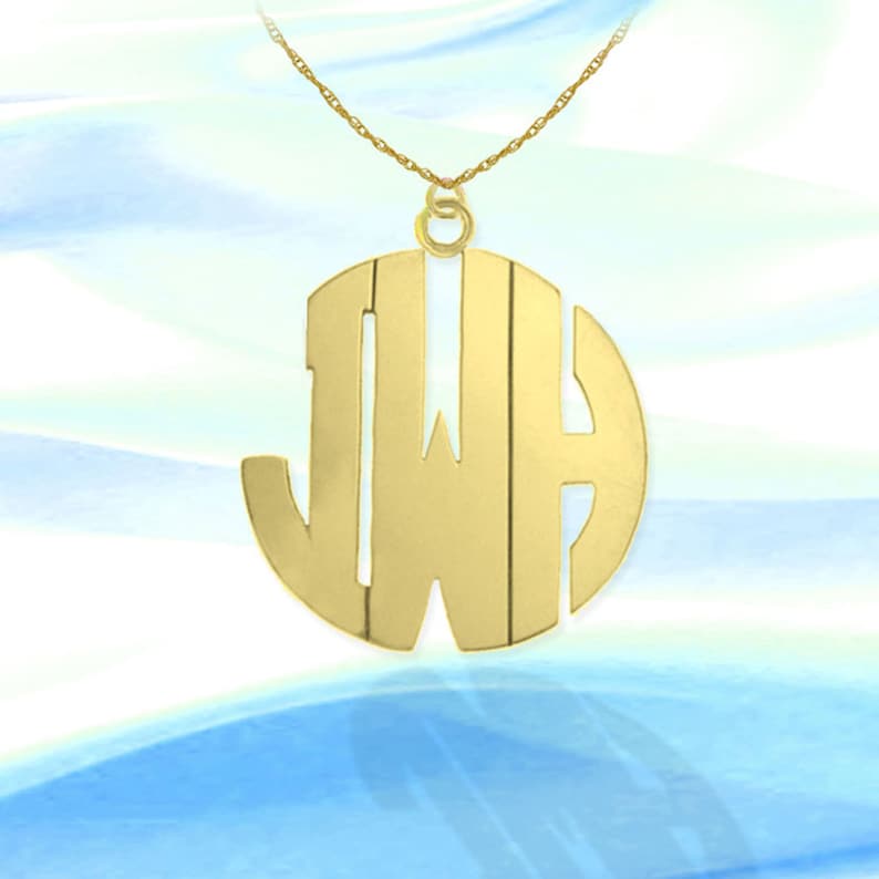 Puede incluir: Un collar de tono dorado con un gran colgante redondo que presenta las iniciales JWH en un estilo de monograma.