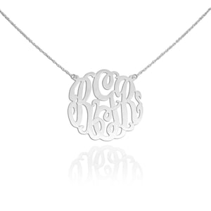 May include: A silver necklace with a large, circular pendant featuring a monogram with the letters "C", "D", and "R" in a cursive script.