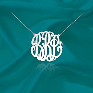 May include: A silver necklace with a large, circular monogram pendant featuring the letters B, R, and P in a cursive script.