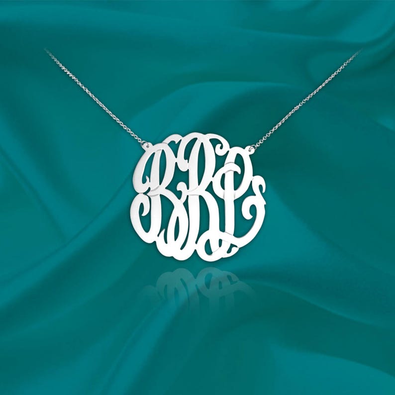 May include: A silver necklace with a large, circular monogram pendant featuring the letters B, R, and P in a cursive script.