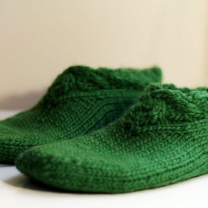 May include: A pair of green knitted slipper socks with a cable knit pattern.