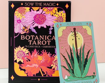 May include: A Botanica Tarot card deck and guidebook set. The black box features floral illustrations and the text "Sow the Magic" and "Botanica Tarot". A single card shows an aloe vera plant and the text "Ace of Wands".