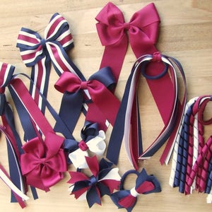 May include: A collection of hair bows and ponytail holders in navy blue, burgundy and white. The bows are made of satin ribbon and the ponytail holders are made of braided ribbon.