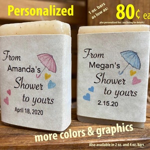 Pode incluir: Dois sabonetes personalizados de 1 on&ccedil;a com um tema de chuveiro. Os sabonetes s&atilde;o embrulhados em papel branco com um design de guarda-chuva rosa e azul. O texto nos sabonetes diz "From Amanda's Shower to yours April 18, 2020" e "From Megan's Shower to yours 2.15.20".