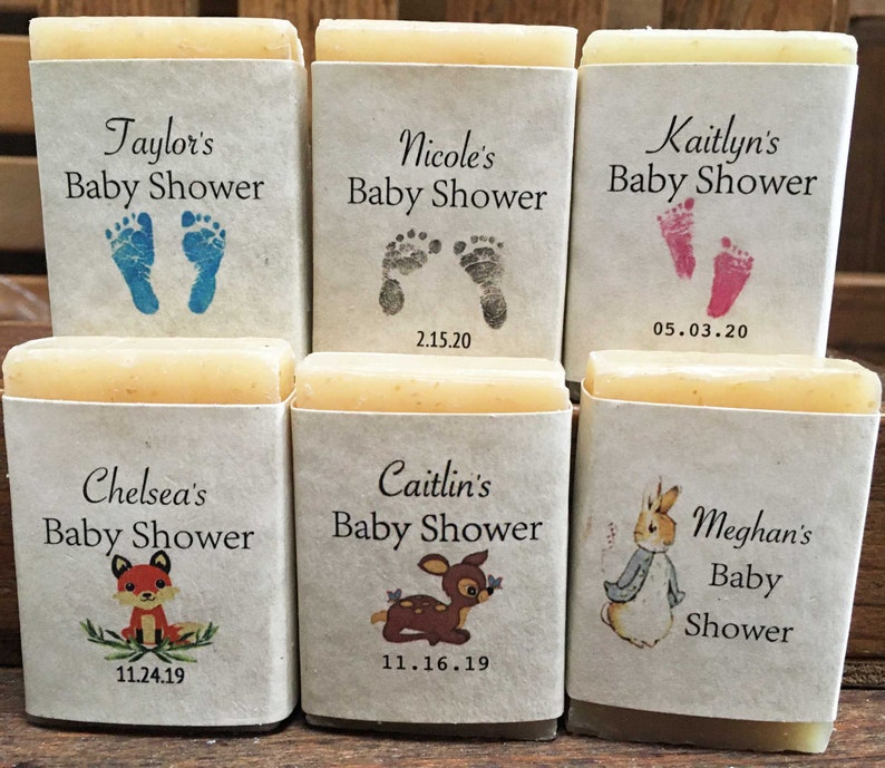 Pode incluir: Seis pequenas barras de sabonete embrulhadas em papel branco com etiquetas personalizadas para um ch&aacute; de beb&ecirc;. As etiquetas apresentam diferentes designs, incluindo pegadas, uma raposa, um veado e um coelho. As etiquetas tamb&eacute;m incluem os nomes das pessoas que est&atilde;o sendo celebradas e as datas de seus ch&aacute;s de beb&ecirc;.