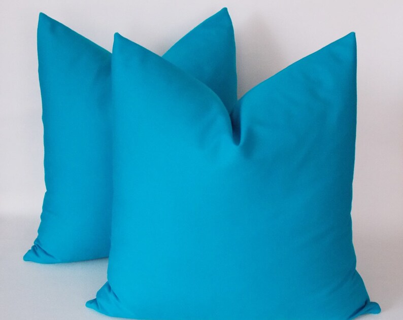 May include: Two turquoise blue throw pillows with a square shape and a smooth fabric texture.