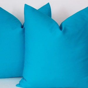 May include: Two turquoise blue throw pillows, made of a soft, smooth fabric. The pillows are arranged side by side, with the front of each pillow facing the viewer.