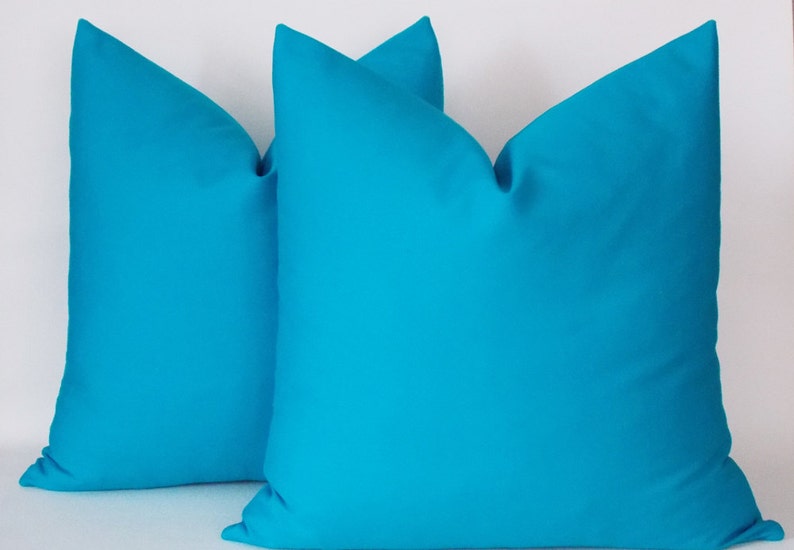 May include: Two turquoise blue throw pillows, made of a soft, smooth fabric. The pillows are arranged side by side, with the front of each pillow facing the viewer.