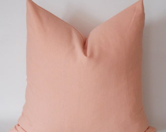 May include: A peach-colored throw pillow with a simple, square shape. The pillow is made of a soft, smooth fabric.