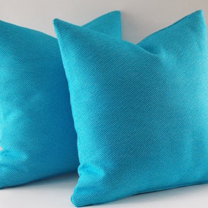 May include: Two turquoise blue throw pillows with a textured fabric. The pillows are made of a soft, woven material.