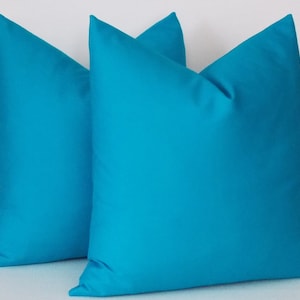 May include: Two turquoise blue throw pillows, made of a soft, smooth fabric. The pillows are arranged side by side, with one slightly overlapping the other.