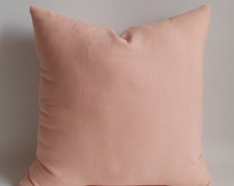 May include: A square peach-colored pillow. The pillow has a soft, textured appearance and is likely made of fabric. The pillow is a solid color and has a simple, minimalist design. The pillow is a decorative item.