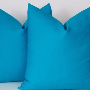 May include: Two turquoise blue throw pillows, made of a soft, smooth fabric. The pillows are square shaped and have a simple, modern design.