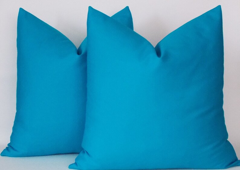 May include: Two turquoise blue throw pillows, made of a soft, smooth fabric. The pillows are square shaped and have a simple, modern design.