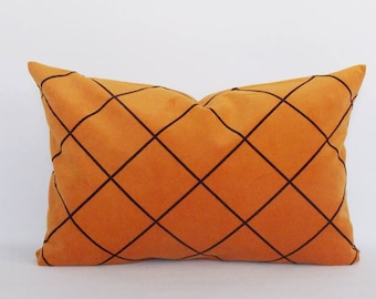 May include: An orange decorative pillow with a black diamond pattern. The rectangular pillow is made of a soft material and is designed for home decor. The pillow is approximately 20 inches long and 12 inches wide.