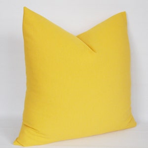 May include: A bright yellow throw pillow with a simple, square shape. The pillow is made of a soft, textured fabric.