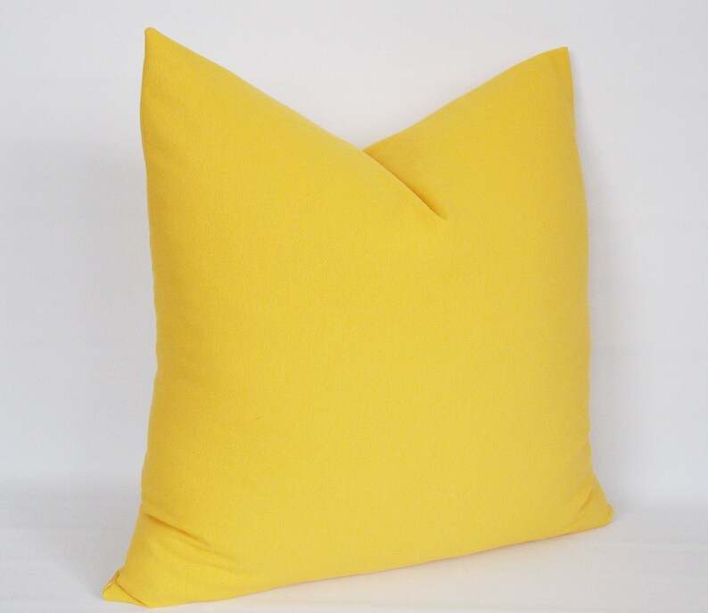 May include: A bright yellow throw pillow with a simple, square shape. The pillow is made of a soft, textured fabric.