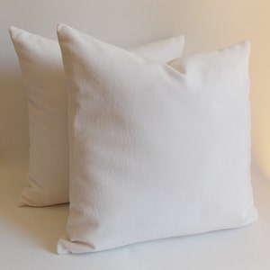 May include: Two white pillow covers, made of a soft, textured fabric. The pillow covers are arranged side by side, with the front of each pillow facing the viewer.