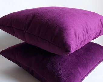 May include: Two purple velvet pillow covers stacked on top of each other. The pillow covers are a deep, rich purple color and have a soft, velvety texture.
