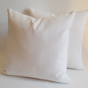May include: Two white pillow covers, made of a soft, textured fabric. The pillow covers are lying flat on a white surface.