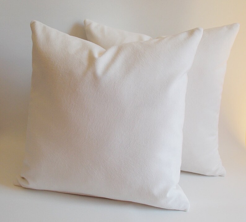 May include: Two white pillow covers, made of a soft, textured fabric. The pillow covers are lying flat on a white surface.