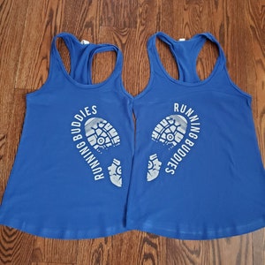 Może przedstawiać: Dwie koszulki bez rękawów w kolorze królewskim z białym nadrukiem śladu buta do biegania i tekstem "Running Buddies".