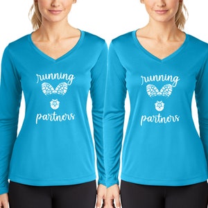 Puede incluir: Dos camisas de manga larga de color azul turquesa brillante con un diseño gráfico blanco. El gráfico presenta dos huellas de zapatos para correr y el texto "running partners".