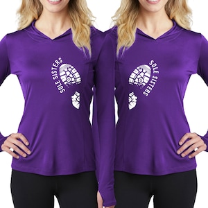 Puede incluir: Dos mujeres con camisas de manga larga de color morado con un gráfico de huella de pie blanco y el texto "Sole Sisters".