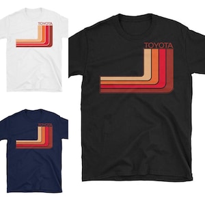 May include: Three t-shirts with a retro-style graphic of the word "TOYOTA" in white letters with a red, orange, and brown striped design. The shirts are available in white, black, and navy blue.