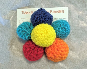 May include: A rainbow crochet flower with six petals in the colors red, orange, yellow, green, blue, and purple. The flower is made from acrylic yarn.