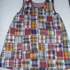 May include: A patchwork dress made from different plaid fabrics in shades of red, blue, yellow, and white. The dress has a sleeveless design and a scalloped neckline.