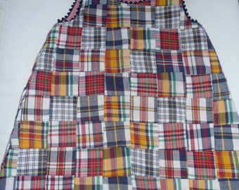 May include: A patchwork dress made from different plaid fabrics in shades of red, blue, yellow, and white. The dress has a sleeveless design and a scalloped neckline.