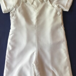 May include: White short-sleeved romper with a collared shirt top and button closures. The romper has a bib-style front with two pockets.