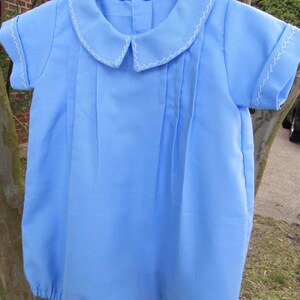May include: A light blue baby onesie with white stitching around the collar and sleeves. The onesie has a Peter Pan collar and is made of a soft, comfortable fabric.