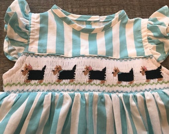 May include: A white and light blue striped dress with a smocked bodice featuring a row of black dogs. The dress has short, ruffled sleeves.